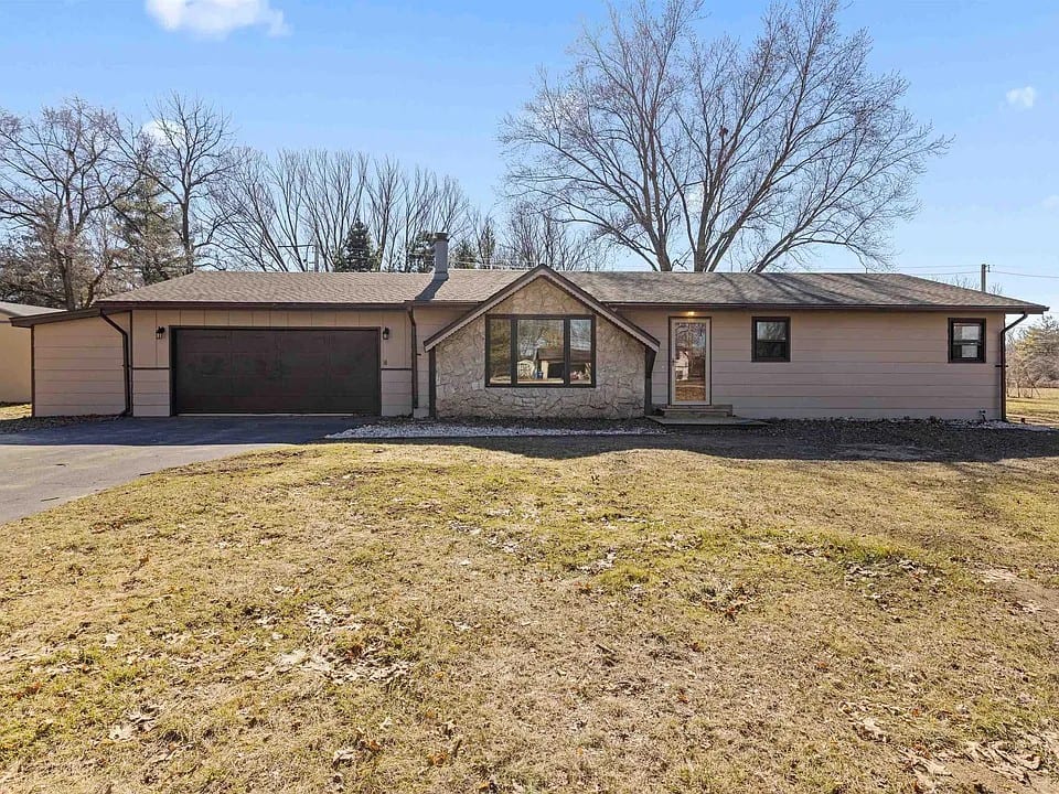 A long single-storey ranch with a stone-faced front gable, dark window trim and an attached two-car garage on an open lot.