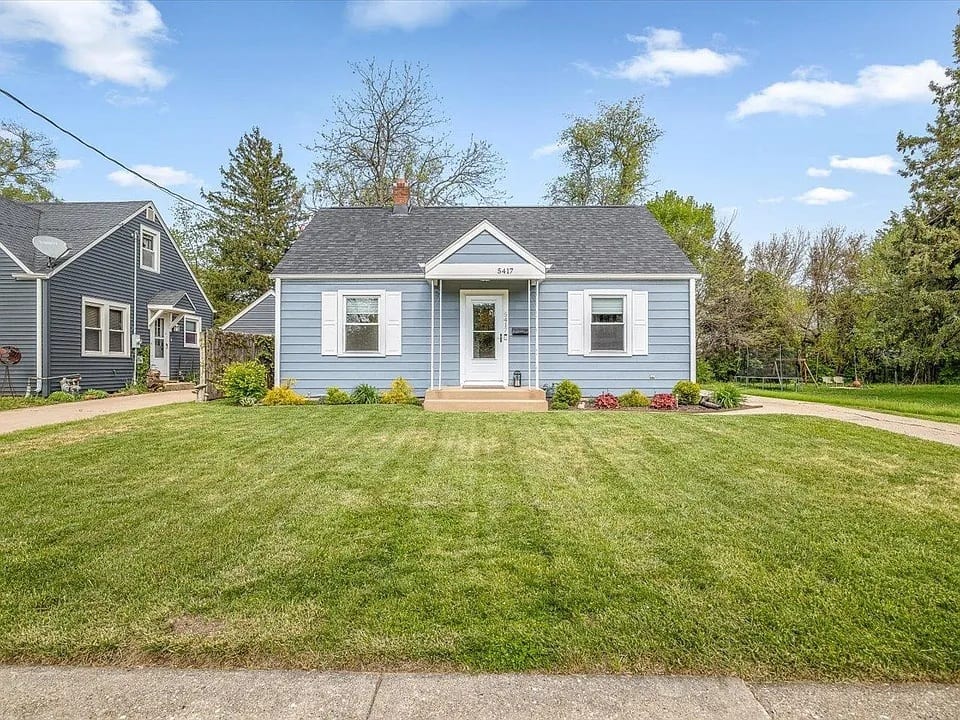 A light blue Cape Cod with white shutters, a gabled entry portico and the number 5417 mounted above the front door.